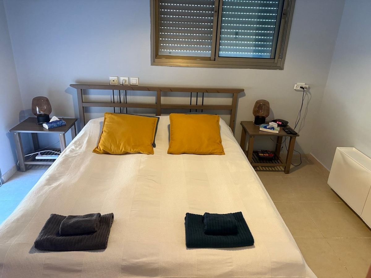 Freshly made double bed with yellow cushions and folded towels